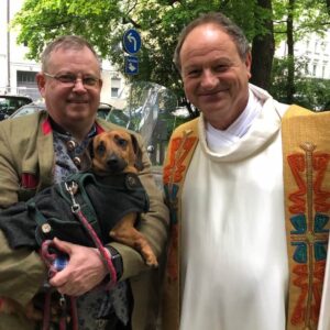 Dackel Franze und Begleiter in Tracht mit Pfarrer Schiessler in München vor der Pilgerreise nach Rom zur Segnung.
